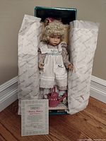 Porcelain doll in original box with protective tissue paper and certificate of authenticity.