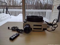 Kodak Ektagraphic Slide Projector AF 2 on table with wired remote and slide tray, snow visible outside through window.