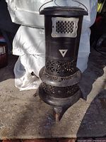 Front view of the black Perfection oil heater showing ventilation holes, handle, and triangular emblem