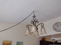Photo of ceiling-mounted metal and ceramic light fixture with three bell-shaped frosted glass shades suspended by decorative chain and scrollwork.