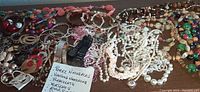 Top-down view of assorted pearl necklaces, colorful beaded necklaces, metallic bracelets and bangles, various styles of earrings, rings, and two wrist watches with black bands, laid out on wooden surface.