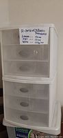 Two white plastic storage drawer units stacked, each with three drawers, translucent fronts with white frames.
