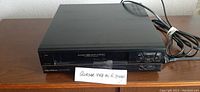 Black Quasar VHS Hi-Fi Stereo VCR front view showing tape loading slot and control buttons.