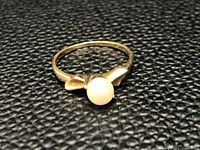 View of vintage 10Kt gold ring with a round white pearl centerpiece on textured black surface.