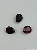 Three pear-shaped garnet gemstones on white background showing faceted cuts and coloration.