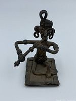 Front angled view of bronze bronze African musician flute player statue figure showing detailed facial features, flute held with arms extended, and seated position on rectangular base.