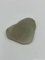 Close-up front view of a light green jade stone pendant carved with subtle patterns showing natural stone texture and slight wear.