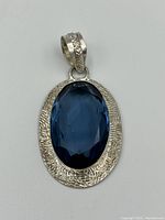 Front view of pendant showing large faceted blue oval stone set in textured sterling silver.