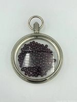 Front view of the round metal pocket watch case filled with garnet beads under transparent glass.