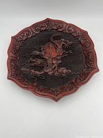 Top view of the red lacquered wooden plate with carved deity riding dragon in center and ornate border