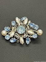 Front view of a vintage brooch with light blue rhinestones and faux pearls in floral arrangement on silver-tone metal.