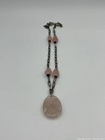 Full necklace laid flat showing the chain with rose quartz beads and carved pendant.