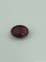 Top view of the oval-shaped ruby showing its deep red color and faceted surface with visible inclusions and surface wear.