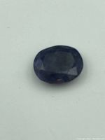 Close-up photo of the oval faceted blue sapphire gemstone lying flat, showing color and cut.