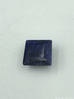 Top-down view of square cut sapphire gemstone showing its shape and surface wear.