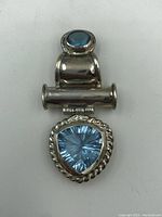 Front view of sterling silver pendant with large triangular blue topaz, twisted rope bezel, and smaller oval blue topaz on bail.