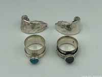 Photo of two sterling silver hammered clip-on earrings and two spinner rings, one with turquoise and one with black stone set in floral engraved band.
