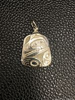 Close-up photo of the sterling silver pendant showing detailed First Nations engravings on a textured background.