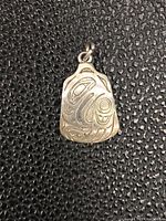Front side of pendant showing First Nations style engraved design with abstract shapes and animal motifs.