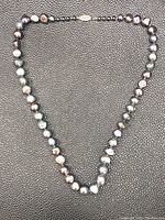 Full view of Tahitian black pearl necklace laid flat, showing the length and irregular pearl shapes.
