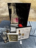 Photo showing three pieces of framed artwork, clear glasses, white hangers and red stirrers on a blue surface outdoors.
