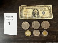Photo shows one worn 1935 Series D United States $1 Silver Certificate and six coins: three US Eisenhower dollars from 1972 and 1973, one bicentennial Kennedy half dollar, and two Mexican peso coins.