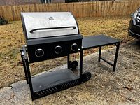 Full side view of the collapsible outdoor grill showing stainless steel lid, control knobs, foldable side table, wheels, and metal frame.