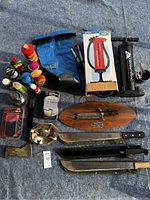 Survival lot items laid out on blue ground cover showing machetes, Buffalo Bill knife plaque, hand pumps, containers, hatchet, folding knife, dry bag, and miscellaneous items.
