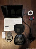 White HP laptop open, Xbox Elite 2 controller in case, wireless fast charger, and phone light ring on floor.
