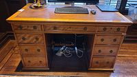 Front view of antique desk showing leather inlaid top, central drawer, and multiple drawers on either side with metal ring handles.