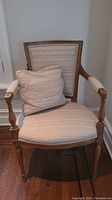 Front view of wooden armchair with light beige patterned upholstery and matching cushion on the seat.