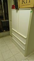 Side view of white baby wardrobe with 3 drawers and 2 doors in a basement setting.