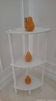 White corner wooden stand in corner with three amber-orange pear-shaped candles placed on shelves