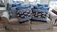 Seven assorted blue and white cushions arranged on beige couch in natural light