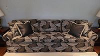 Full front view of the three-seater sofa showing the tropical leaf upholstery and four accompanying throw pillows.