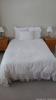 Double bed made with white bedding including pillows and pillow shams, flanked by two wooden nightstands each with a lamp.