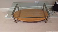 Top view of coffee table showing thick beveled glass top and oval wooden lower shelf supported by metal frame.