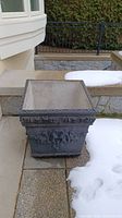 Front exterior view of square planter on patio with decorative motifs.