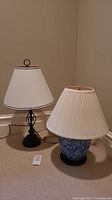 Photo showing both lamps side by side: black metal spiral lamp with white shade, and blue and white porcelain lamp with pleated shade.