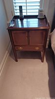Front view of a wooden nightstand showing two doors, drawer on top, polished brown finish, with items placed on top.