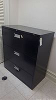 Front and side view of black three drawer metal file cabinet with key lock visible on top drawer
