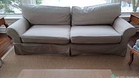 Full frontal view of sofa showing rolled arms, skirted base, cushions and slipcover