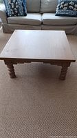 Front view showing solid wood square coffee table with twisted legs and visible wear on surface.