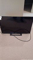 Front view of Sony 32 inch TV on stand without power on, showing black screen and power cable on carpet.