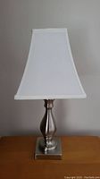 Full view of one metal table lamp showing the white shade and brushed metal base on a wooden surface.
