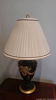 Front view of lamp with white pleated shade and black and gold porcelain base