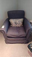 Front view of grey blue upholstered armchair with down filled cushions and a decorative leaf-patterned pillow on the seat.