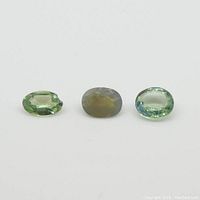 Three oval chrysoberyl gemstones laid flat on a white surface showing color and shape.
