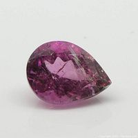 Close-up of pear-shaped pink tourmaline gemstone showing facets and internal features on white background.