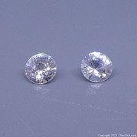 Two round clear white zircon gemstones placed side by side on a flat surface.